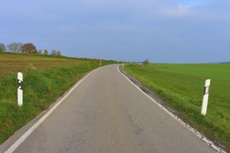 Lonely country road through green fields under a cloudy sky, Hornbach, Walldürn, Odenwald,