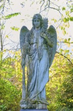 Angel made of stone with sword in an autumnal setting, surrounded by colourful leaves, cemetery,
