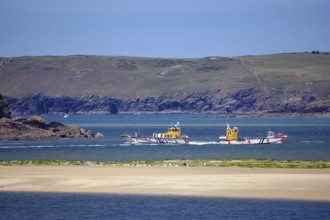 Two small passagi in blue water against a rocky coastline and green cliffs, Camel Trail, Padstow,