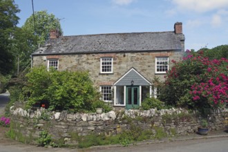 Stone house with lush garden and blooming flowers under a blue sky, idyllic cottage, Cornwall,
