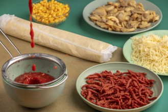 Tomato sauce drips into a sieve alongside other ingredients for pizza