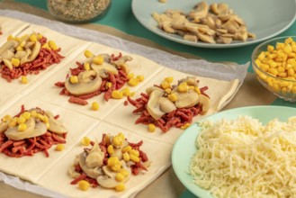 Sliced dough squares with tomato paste, bacon, mushrooms and sweetcorn alongside other ingredients
