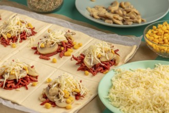 Sliced dough squares with tomato paste, bacon, mushrooms, sweetcorn and cheese alongside other