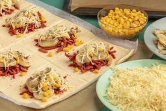 Sliced dough squares with tomato paste, bacon, mushrooms, sweetcorn, cheese and oregano alongside