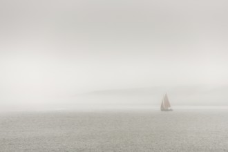 A sailing boat is travelling on the ocean on a cloudy day. The sky is overhanging and the water is
