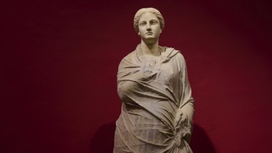 Marble statue of a woman in draped shawls, depicted against a red background, Archaeological