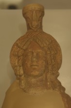 Ancient stone figurine head with elaborate hairstyle, placed on an exhibition shelf, sun disc,