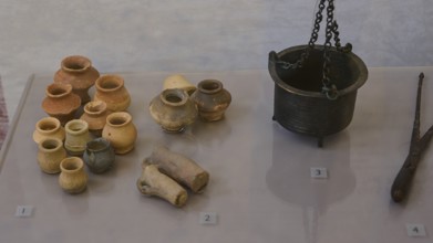 Collection of ancient ceramic artefacts, various pots and a metal crucible on display,