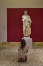 Woman observing an ancient marble statue of a man in a museum, Archaeological Museum, Kos Town,