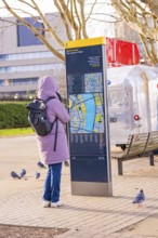 Woman in warm clothes looking at a map at a city map kiosk, pigeons on the ground, London, United