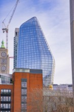Modern building with glass façade and construction crane under blue sky, London, United Kingdom,