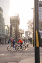 Two cyclists ride on an urban road, sunlight reflected on the buildings, London, United Kingdom,