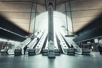 Modern escalators in a train station with symmetrical design and bright lighting, Canary Wharf