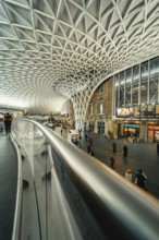 Wide angle view of a busy train station with glass roof and escalators, King's Cross Station,