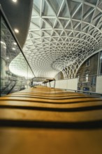 View along a bench under an expansive, modern glass roof in the train station, King's Cross