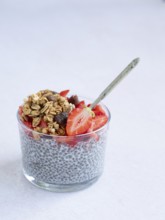 Chia seed pudding in a glass with fresh strawberries, granola, and a spoon, representing healthy