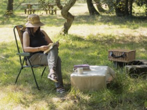 Woman enjoying a peaceful afternoon reading a book in a folding chair under a tree