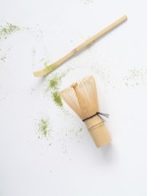 Matcha tea ceremony tools with scattered green powder on white background