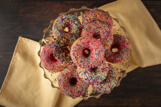 Donuts with colorful sprinkles on a glass plate, presented on a wooden table with yellow cloth