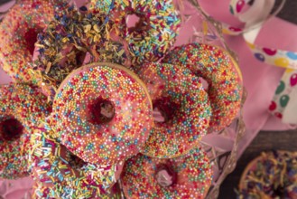 Colourful donuts with sprinkles and streamers on pink cloth, carnival
