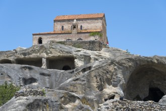 Church on a rock with caves below and ancient architecture against a blue sky, 10th century