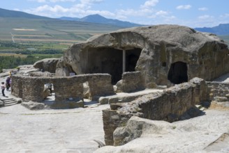 Ancient cave system with ruins in a vast landscape, visitors explore, Tamaris Darbasi, Tamaras