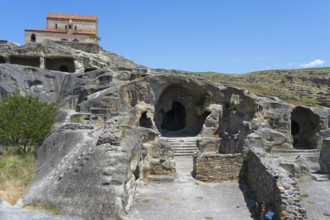 Ancient cave with entrances, dominated by an old building and surrounded by nature, 10th century