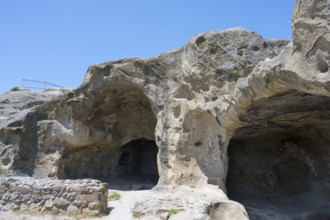 Rock formation with cave entrances under blue sky in natural landscape, Uplistsikhe cave town,