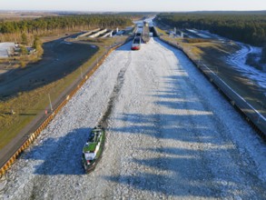 A ship sails through a long, icy waterway lined with locks in a wide landscape, aerial view,