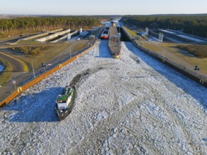 A lock channel with moving ships, frozen in a winter environment with forests, aerial view,