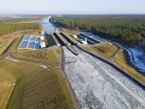 Drone view of a canal in winter with ice, snow-covered soil and adjacent forest, aerial view,