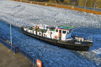 A ship navigates through an ice-covered channel in the harbor area in cold winter weather, aerial