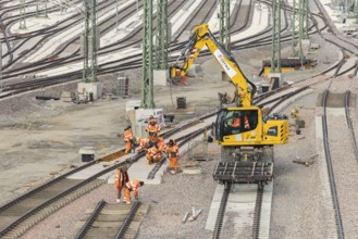 Construction workers work with a crane truck on a section of rail in a large track area,