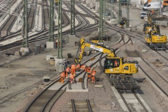 Workers wearing orange safety clothing work on railroad tracks with technical equipment,