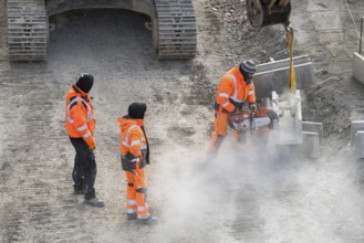 Construction workers in protective clothing work with machines on a dusty construction site,