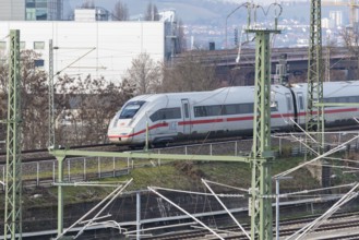 An ICE high-speed train travels on rails through an urban landscape with power poles, Untertürkheim
