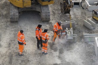 Construction site workers use a power grinder in an urban environment next to an excavator,