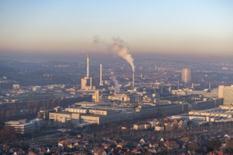 City view at dusk, modern buildings in the foreground, chimneys with smoke and a calm atmosphere in