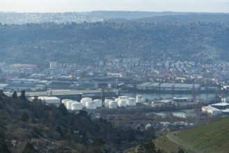 Industrial plant with white tanks in front of a hilly landscape covered with houses, view of