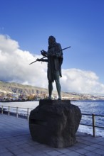 Bronze statue of a man with spear on the coast against blue sky and clouds, Candelaria Tenerife
