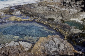 Rocky coast with cave and clear water. Waves and erosion shape the dark rock formations, Yaiza