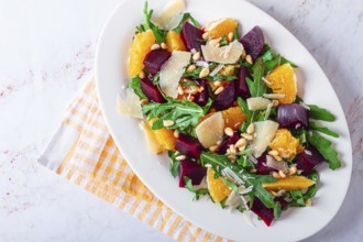 A salad made with chunks of beet, orange slices, and arugula. It is topped with cheese shavings and