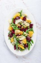 A salad made with chunks of beet, orange slices, and arugula. It is topped with cheese shavings and
