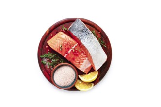 A wooden plate holds two salmon fillets next to lemon slices and a small bowl of salt. Fresh herbs