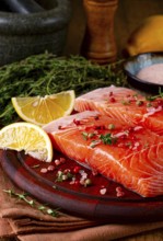 Two salmon fillets rest on a wooden platter. The fillets are garnished with herbs and spices. Lemon