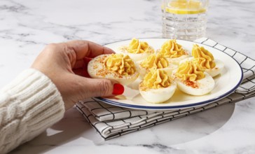 Stuffed eggs with paprika, on a plate, a woman's hand reaches for it