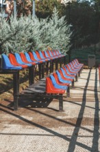 Rows of red and blue stadium seats are neatly arranged in a park. Bright sunlight illuminates the