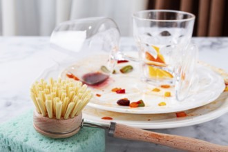 Dishes are stacked on a kitchen counter with food remnants after a meal. A cleaning brush and