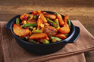 Steakhouse pfanne, fried potato slices, with meatballs, and vegetable mixture, on a black plate