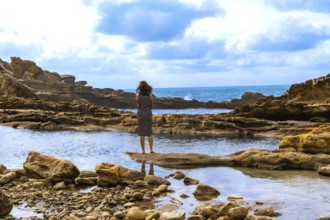 Woman standing on a natural rock formation, looking out at the rugged jaizkibel coast and atlantic